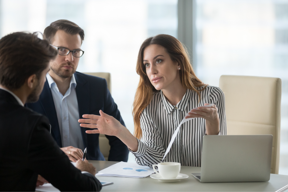 Três pessoas sentadas ao redor de uma mesa de escritório. As pessoas estão com uma expressão de descontentamento. Sinais para ficar alerta.