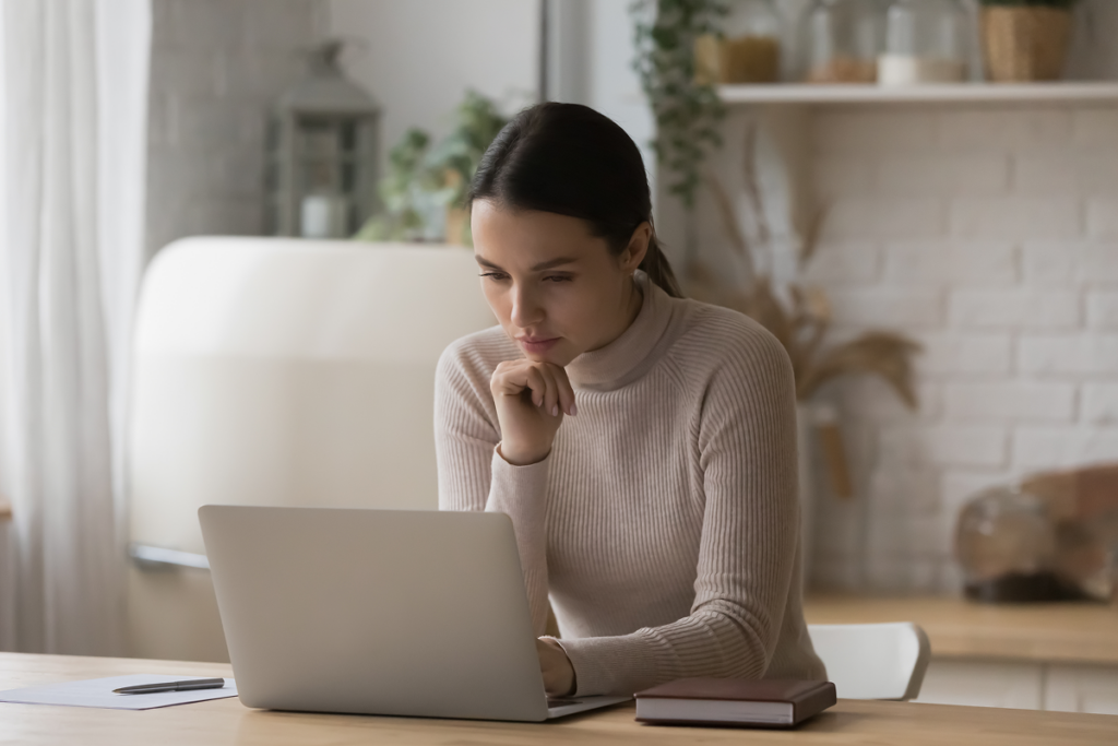 Mulher pensando sentada em sua cozinha e olhando para o computador. Quando posso começar uma pós-graduação