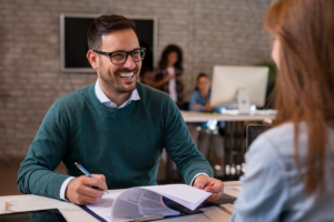 perguntas comuns em entrevistas de emprego. Homem entrevistando mulher e sorrindo.